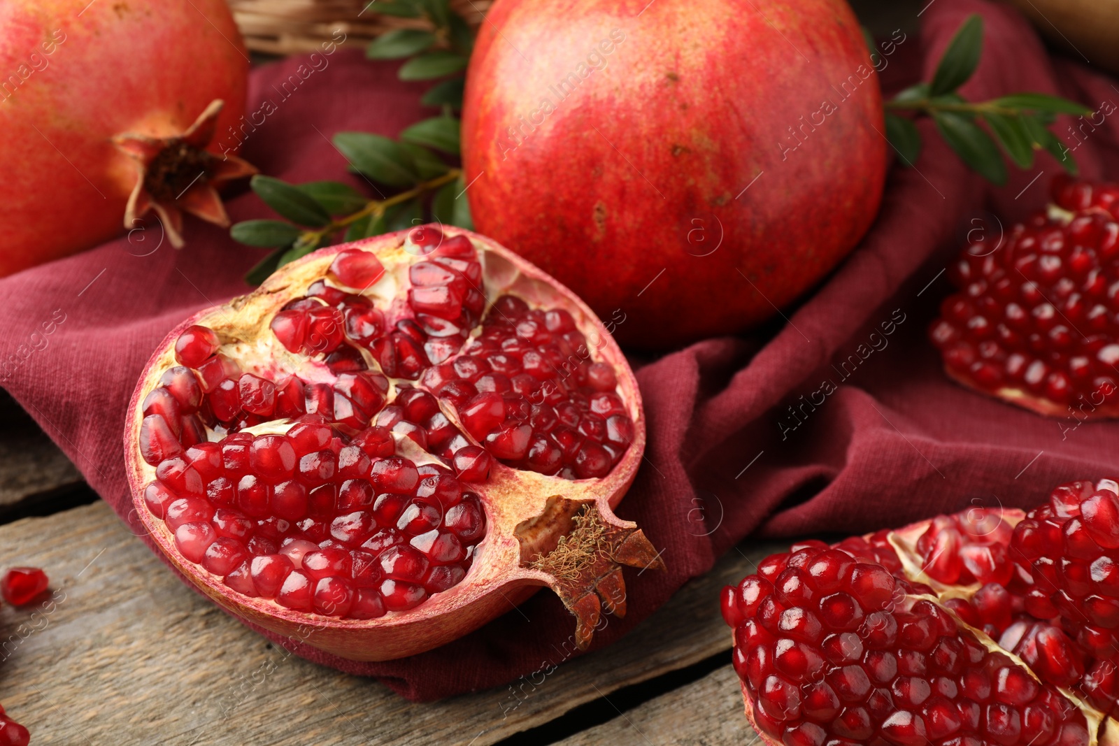 Photo of Fresh pomegranates and green leaves on wooden table, closeup