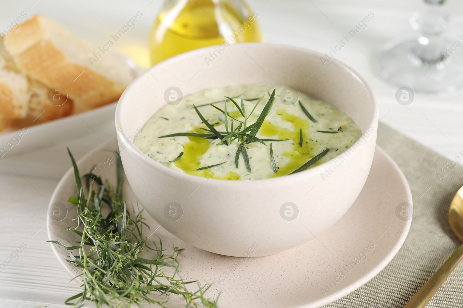 Photo of Delicious cream soup with tarragon, spices and potato in bowl served on white wooden table, closeup