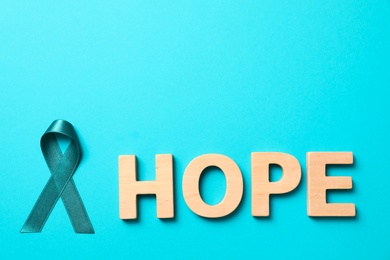 Photo of Word Hope made of wooden letters and teal awareness ribbon on light blue background. Symbol of social and medical issues