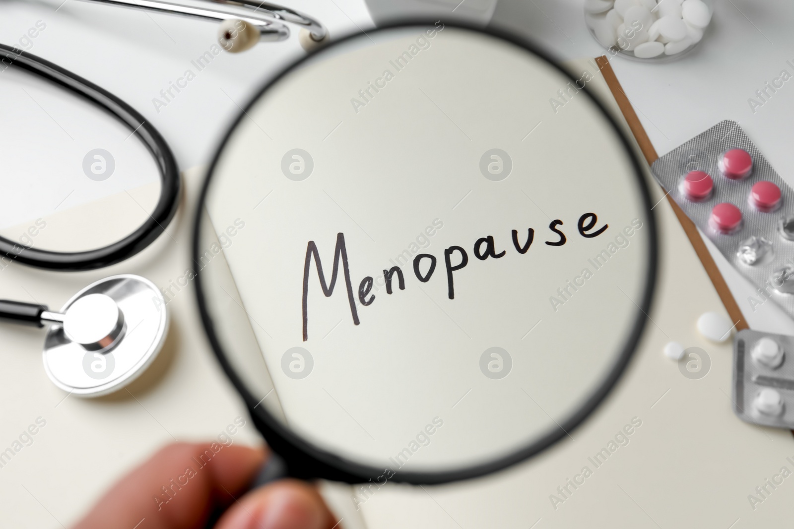 Photo of Woman holding magnifying glass over notebook with word Menopause, closeup