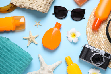 Flat lay composition with sun protection products and beach accessories on light blue background