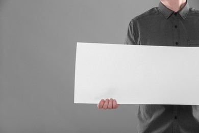 Man holding sheet of paper on grey background, closeup. Mockup for design