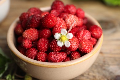 Photo of Fresh wild strawberries and flower in bowl on table, closeup