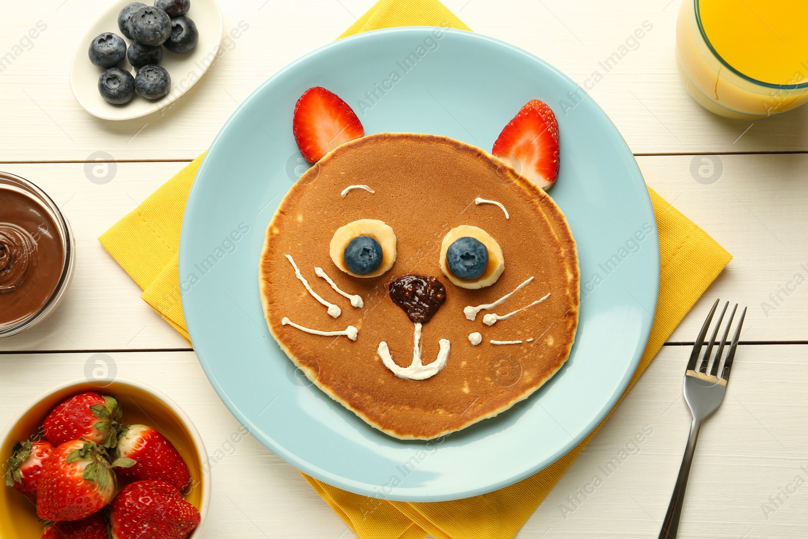 Photo of Creative serving for kids. Plate with cute cat made of pancakes, berries, cream, banana and chocolate paste on white wooden table, flat lay