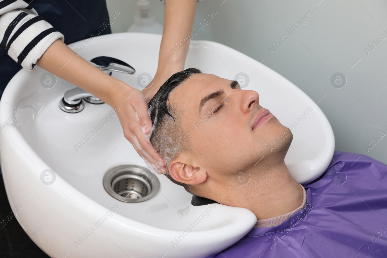 Photo of Professional hairdresser washing client's hair at sink, closeup