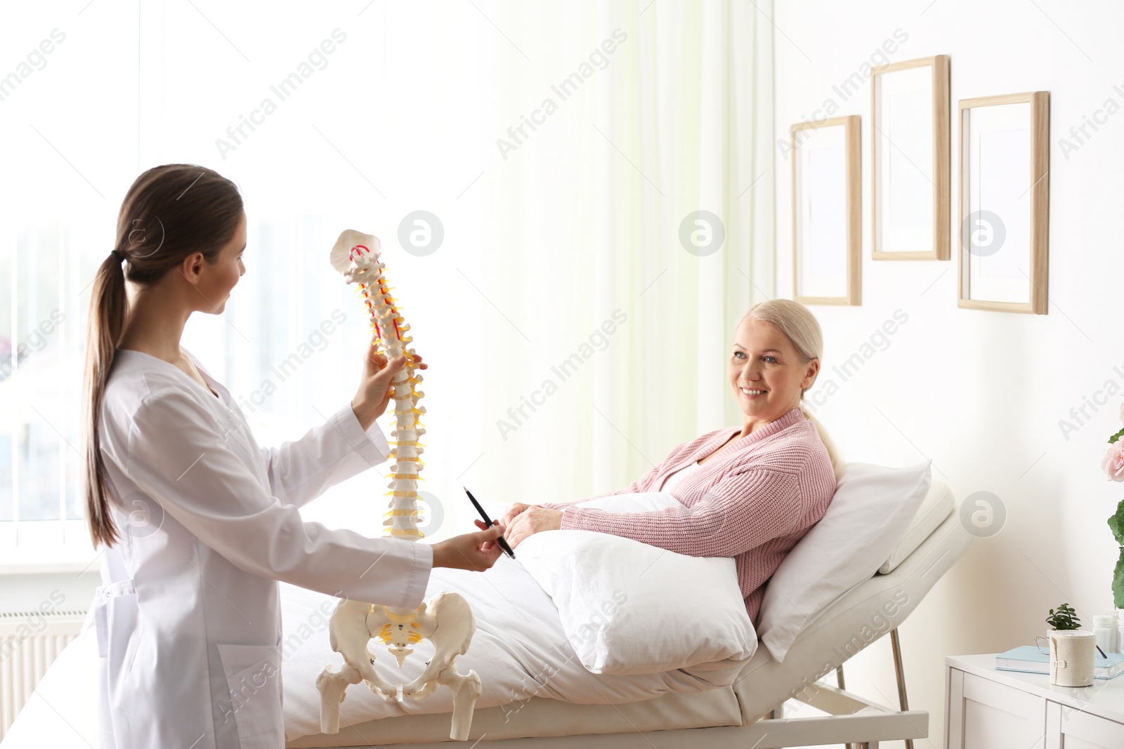 Photo of Female orthopedist explaining structure of spine to patient in clinic