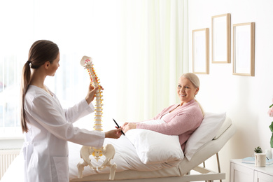 Photo of Female orthopedist explaining structure of spine to patient in clinic