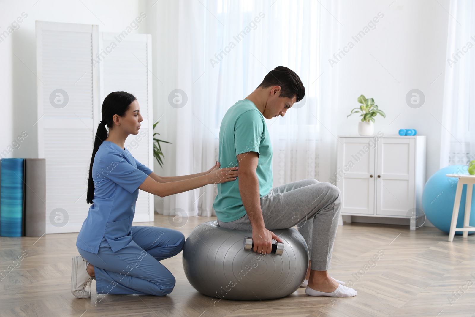 Photo of Orthopedist helping patient to do exercise with dumbbell in clinic. Scoliosis treatment