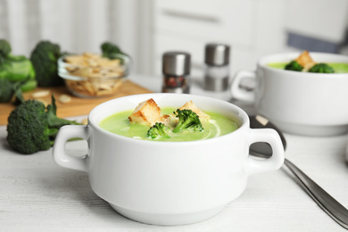 Photo of Delicious broccoli cream soup with croutons served on white wooden table indoors