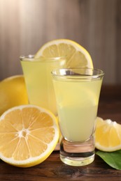 Photo of Tasty limoncello liqueur, lemons and green leaf on wooden table, closeup
