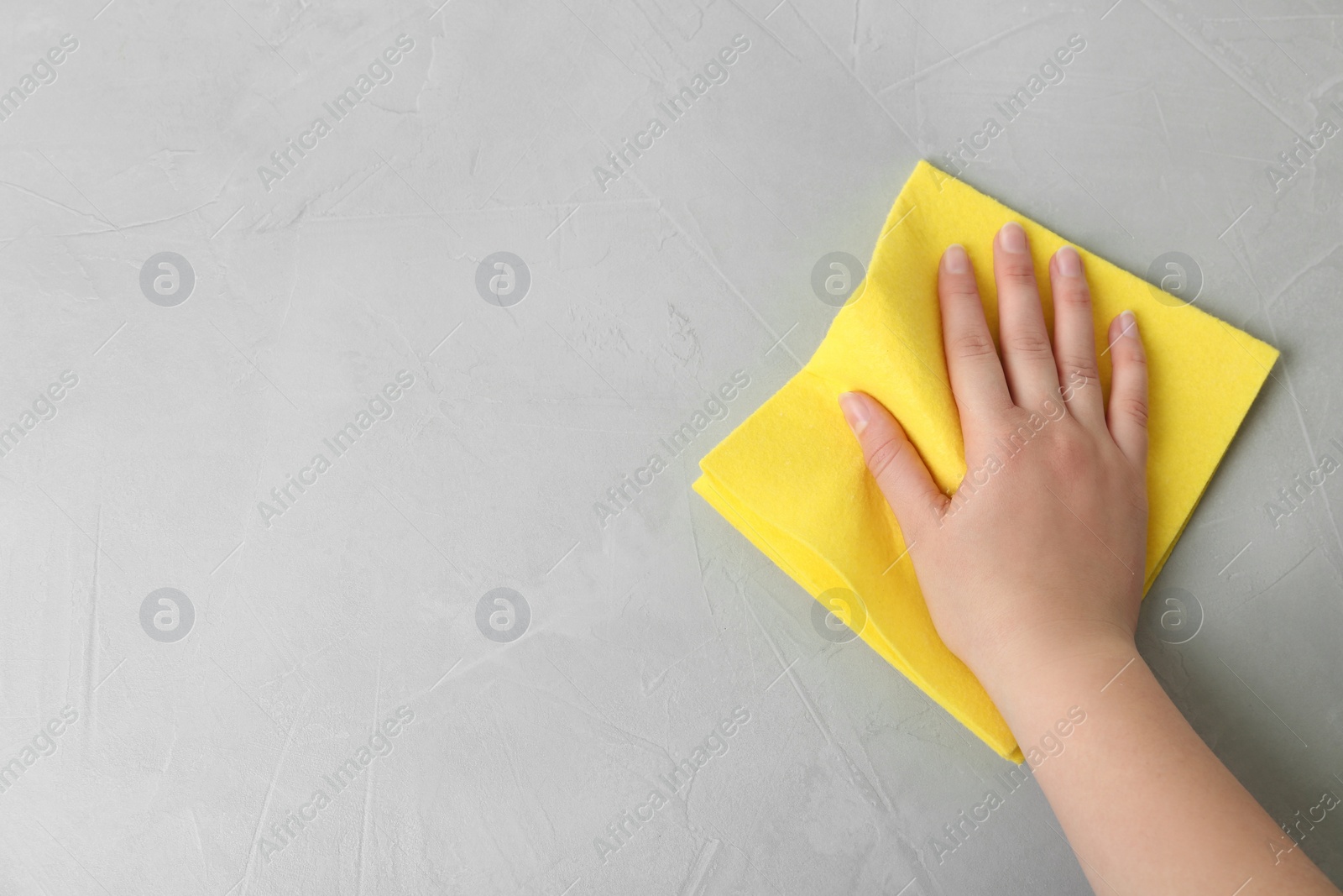 Photo of Woman wiping grey table with rag, top view. Space for text