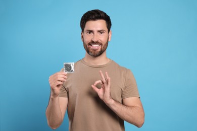 Happy man with condom showing ok gesture on light blue background. Safe sex