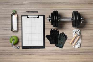 Photo of Clipboard with workout plan, apple and sports equipment on wooden table, flat lay. Personal training