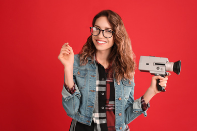 Beautiful young woman with vintage video camera on red background