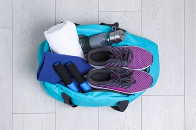 Photo of Bag with different sports equipment on wooden floor, top view