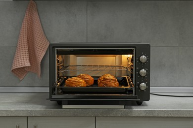 Open electric oven with delicious pastry on grey table in kitchen