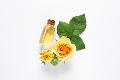 Photo of Bottle of rose essential oil and flowers on white background, top view