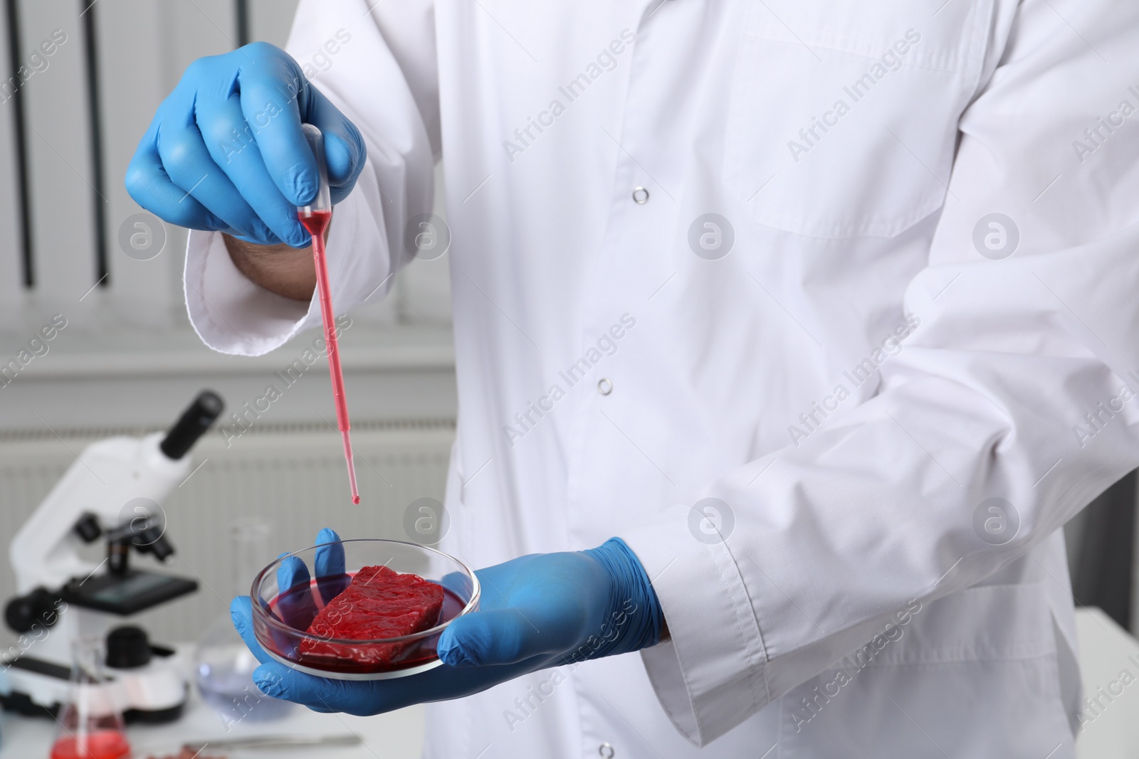 Photo of Scientist dripping red liquid into Petri dish with raw cultured meat in laboratory, closeup