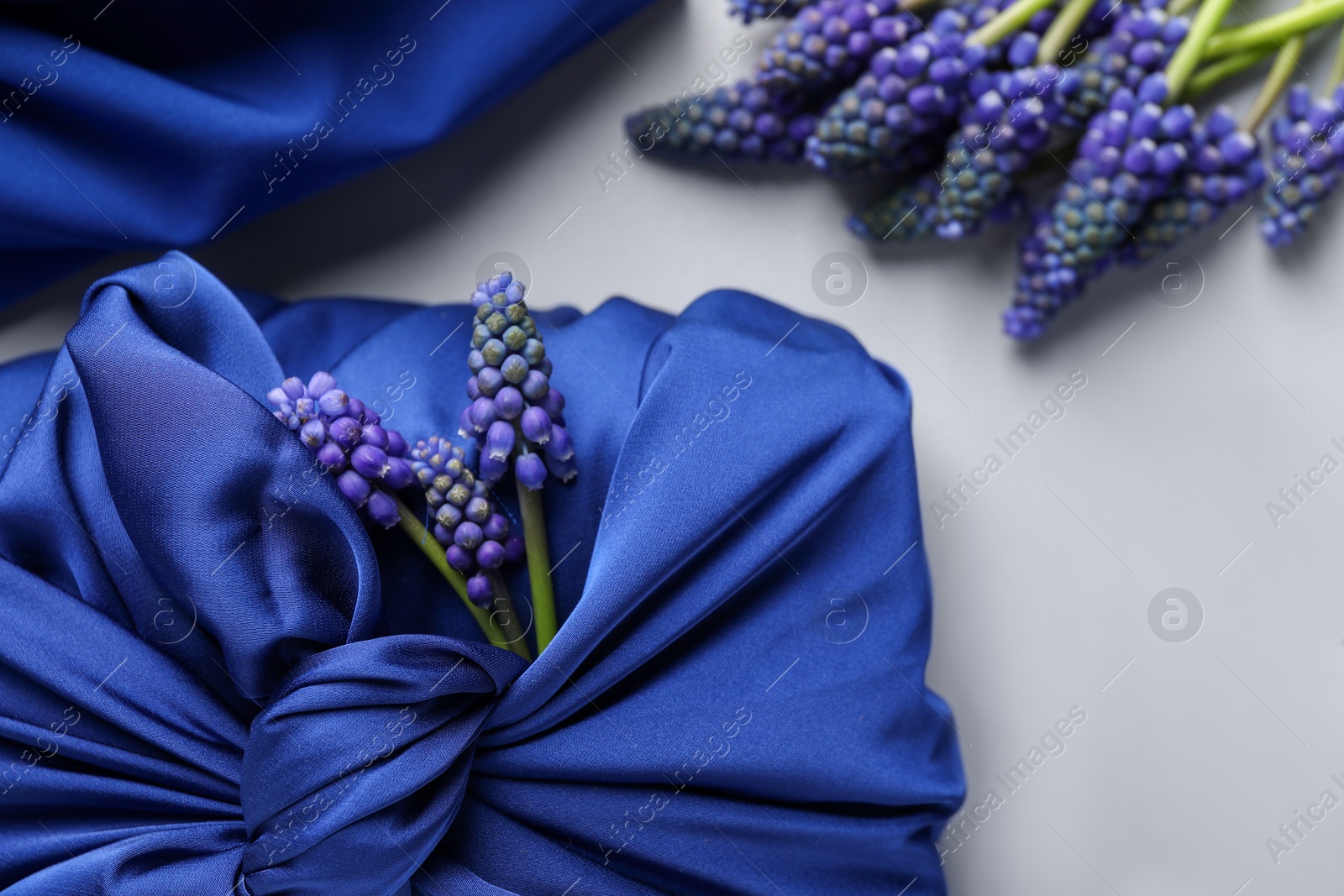 Photo of Furoshiki technique. Gift packed in blue silk fabric, muscari flowers and ribbon on white table, closeup