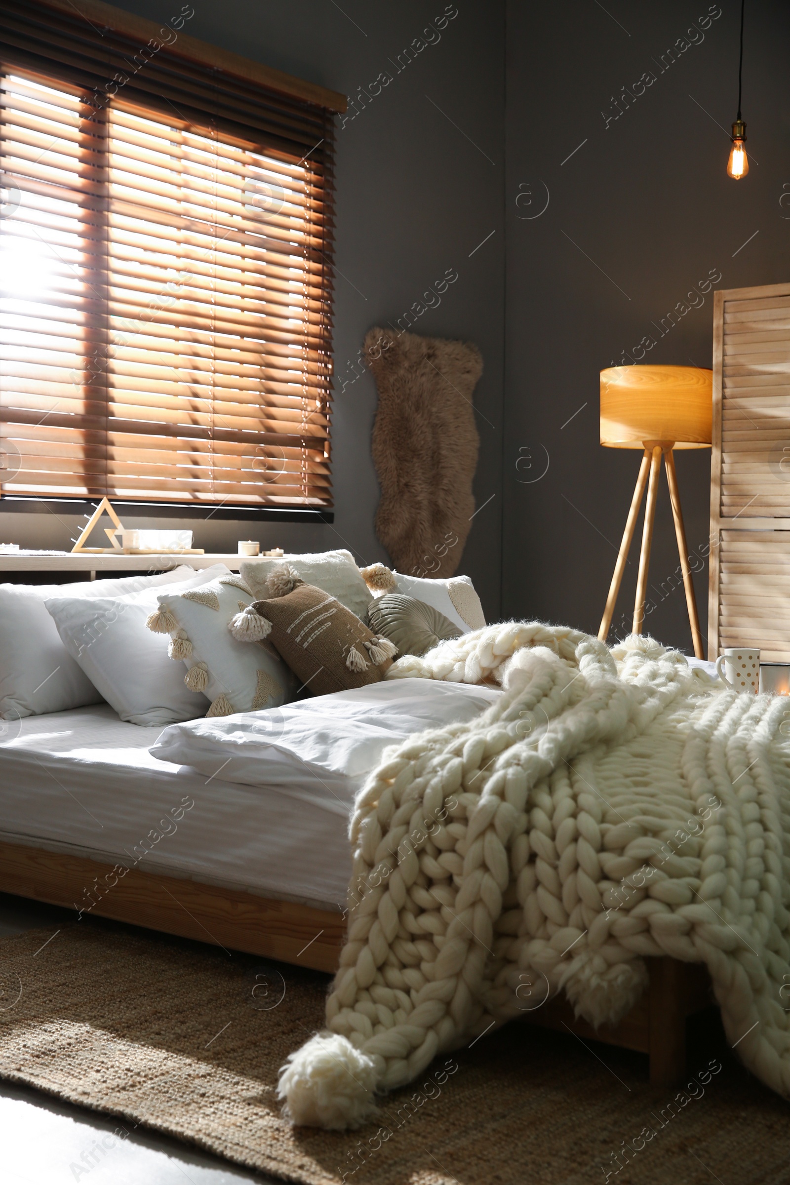 Photo of Cozy bedroom interior with knitted blanket and cushions