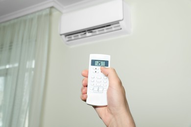 Photo of Man operating air conditioner with remote control indoors, closeup