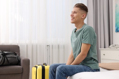 Smiling guest with suitcase relaxing on bed in stylish hotel room. Space for text