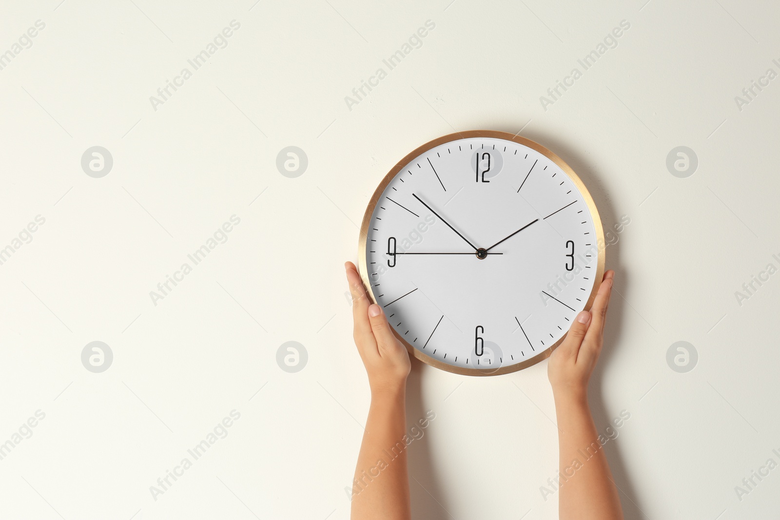 Photo of Woman touching clock on light wall, space for text. Time management