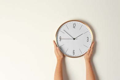 Photo of Woman touching clock on light wall, space for text. Time management