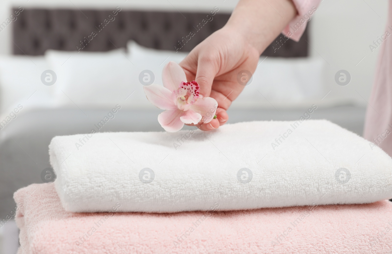 Photo of Woman putting flower on stack of clean towels in bedroom