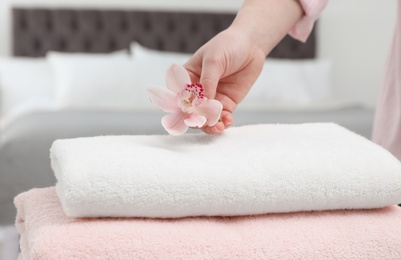 Woman putting flower on stack of clean towels in bedroom