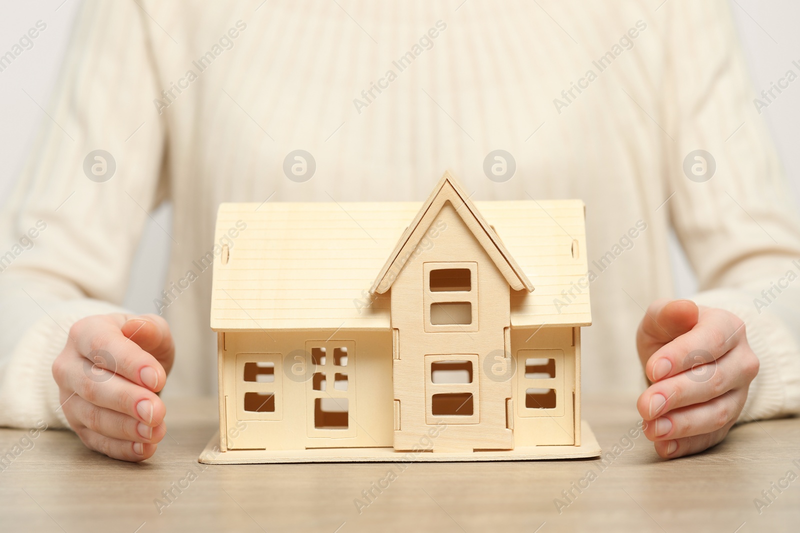 Photo of Home security concept. Woman with house model at wooden table, closeup