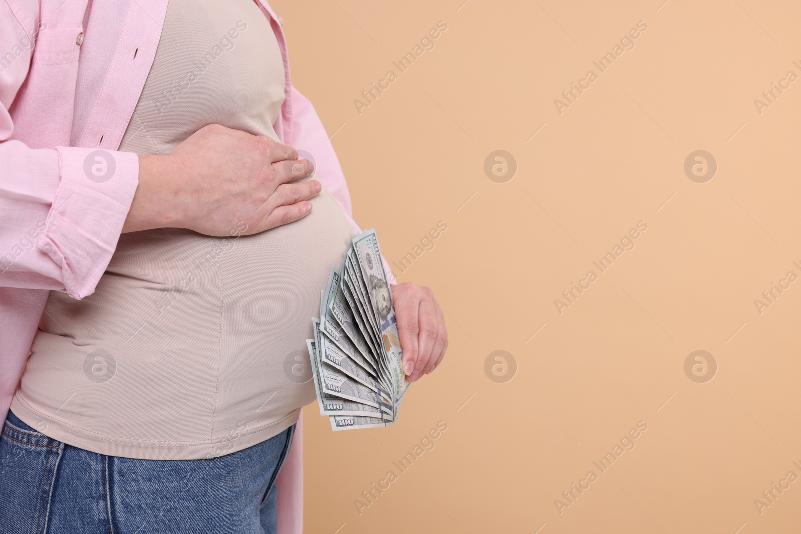 Photo of Surrogate mother. Pregnant woman with dollar banknotes on beige background, closeup. Space for text