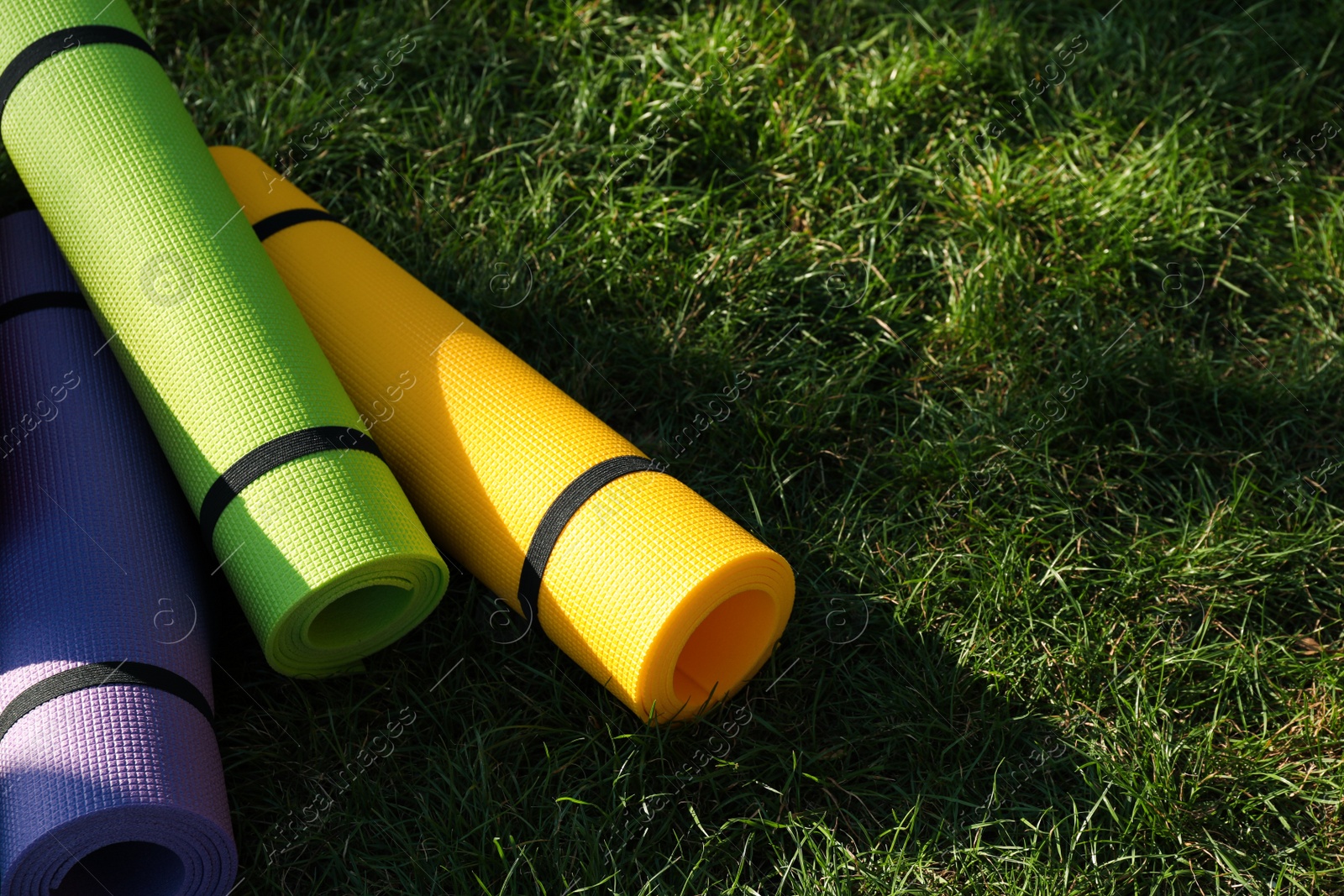 Photo of Bright exercise mats on fresh green grass outdoors, space for text