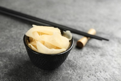 Photo of Spicy pickled ginger and chopsticks on grey table, space for text