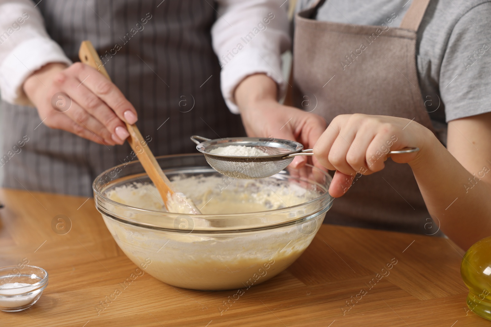 Photo of Making bread. Mother and her daughter preparing dough in bowl at wooden table in kitchen, closeup