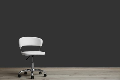 Photo of Comfortable office chair near black wall indoors. Space for text