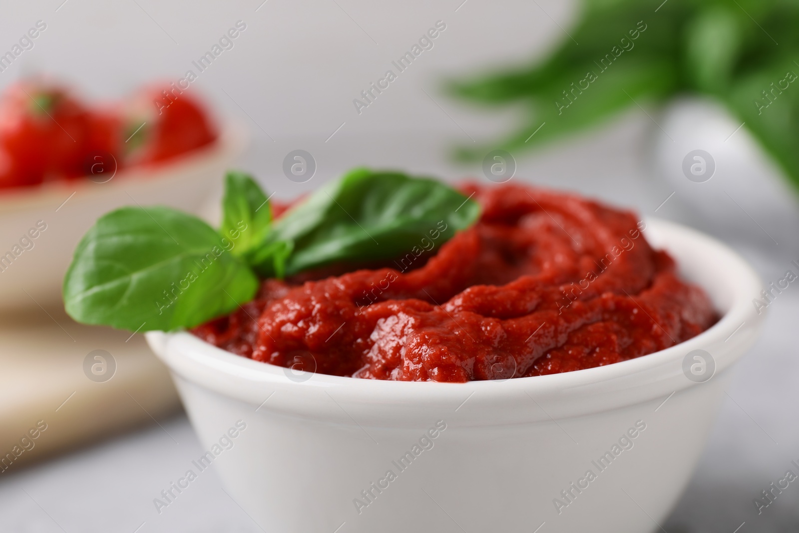Photo of Tasty tomato paste and basil in bowl on table, closeup