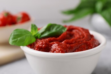 Tasty tomato paste and basil in bowl on table, closeup