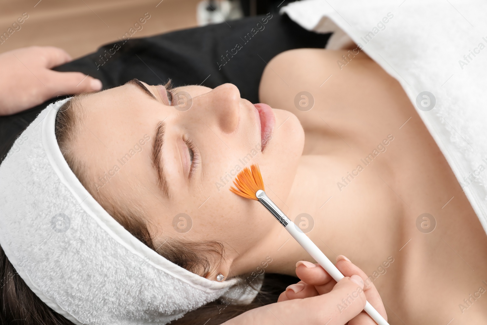 Photo of Cosmetologist with brush applying cosmetic product to client`s face in clinic, closeup