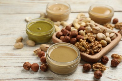 Jars with butters made of different nuts and ingredients on white wooden table, closeup