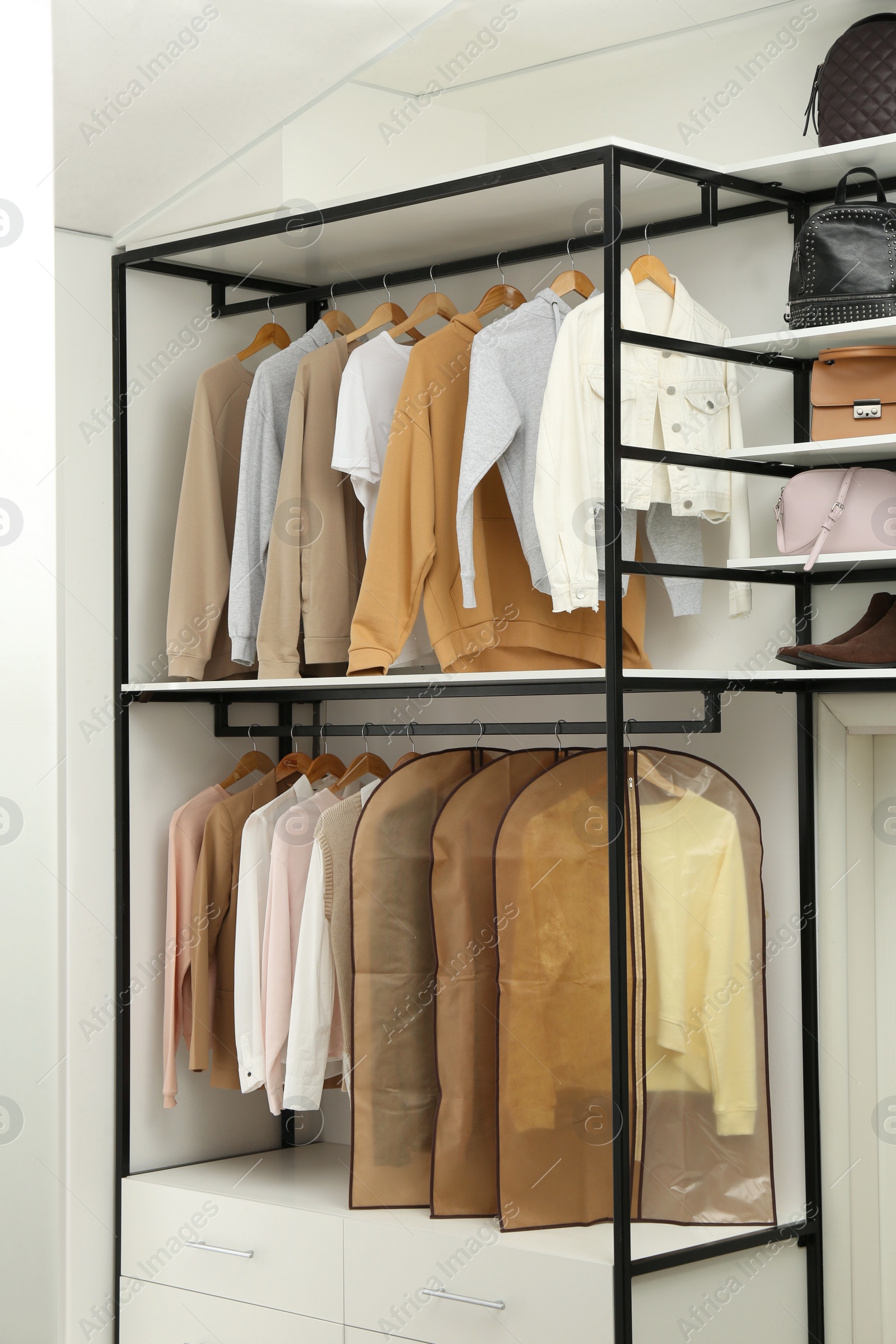 Photo of Garment bags with clothes on rack in dressing room