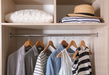 Photo of Collection of stylish clothes and pillow in wardrobe closet