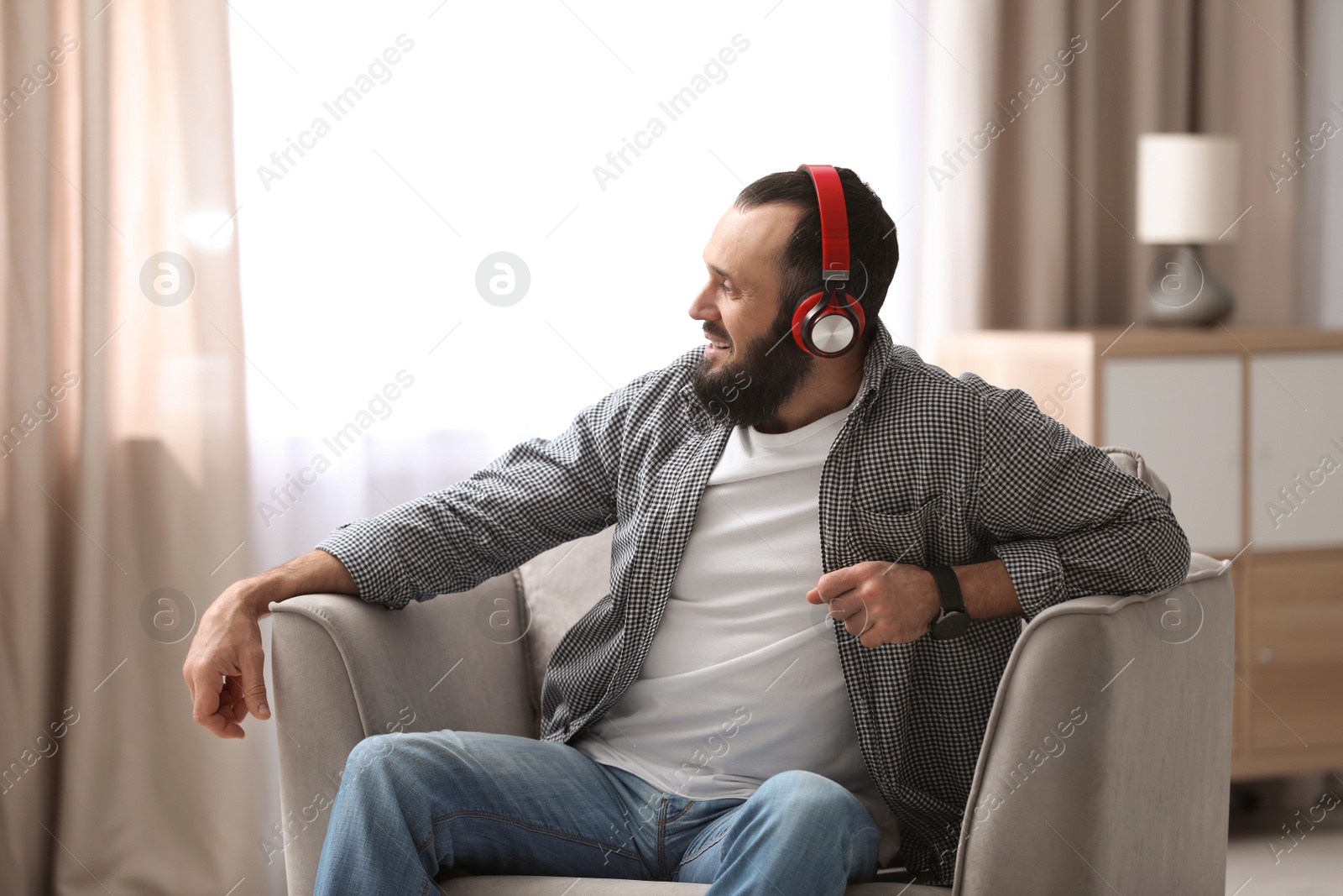 Photo of Mature man with headphones resting in armchair at home