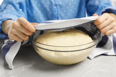 Woman covering fresh yeast dough for cake with kitchen towel at marble table, closeup