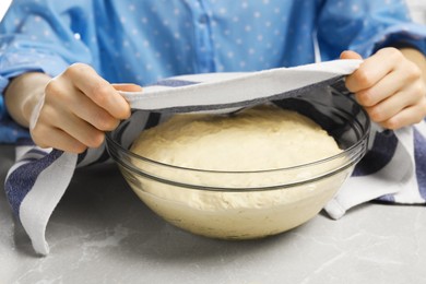 Photo of Woman covering fresh yeast dough for cake with kitchen towel at marble table, closeup