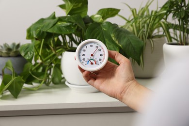 Photo of Woman holding round hygrometer with thermometer near plants indoors, closeup