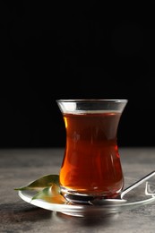 Photo of Glass with traditional Turkish tea on grey table against black background