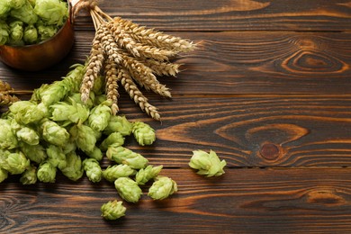 Photo of Fresh hop flowers and wheat ears on wooden table, space for text