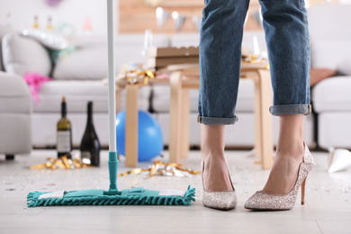Photo of Young woman with mop cleaning messy room after party, closeup of legs