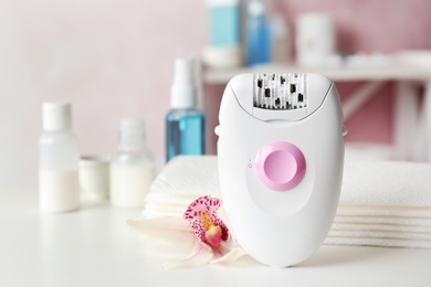 Photo of Modern epilator and beautiful flower on table